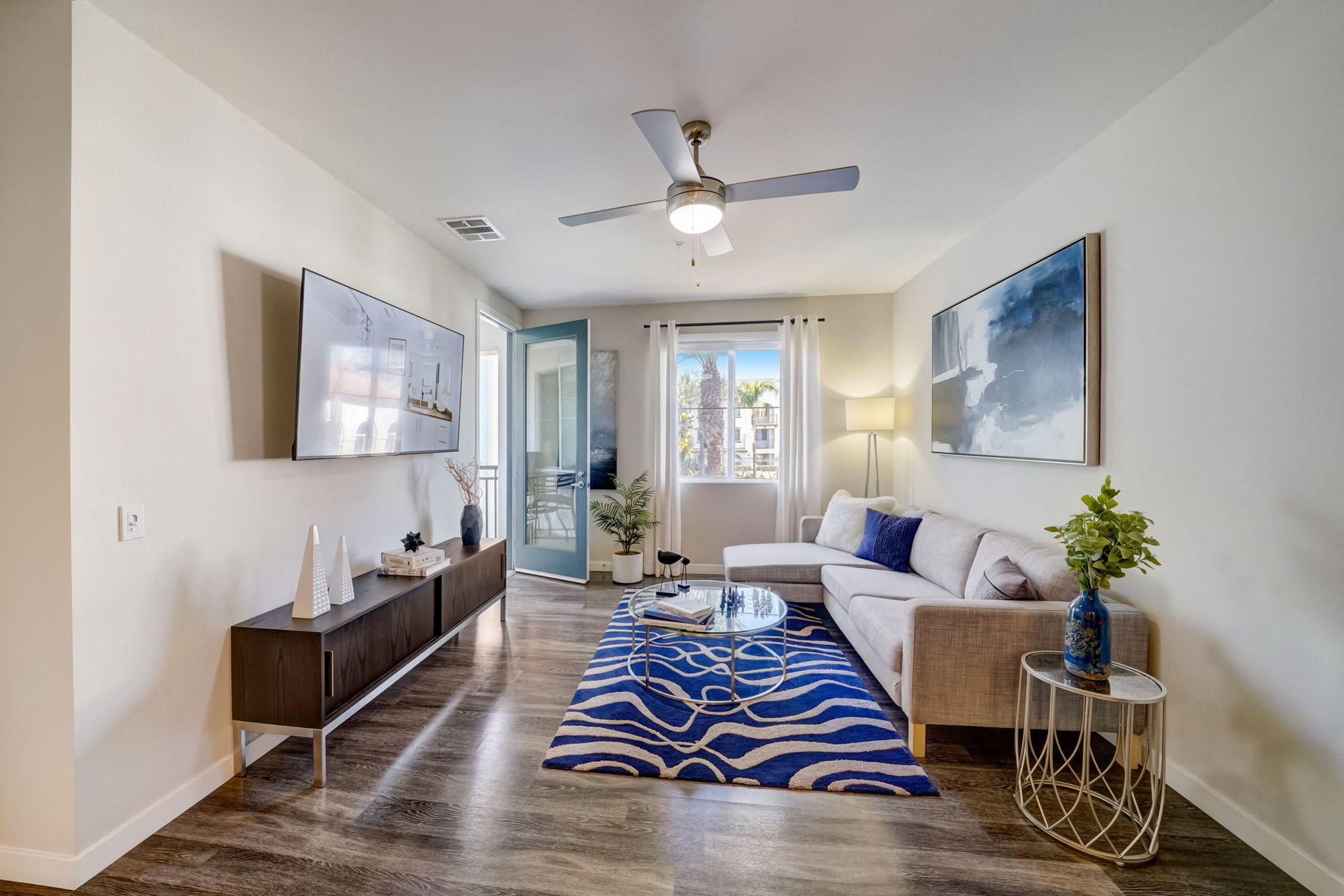 Modern living room at Vistara Apartments featuring a plush couch and ceiling fan, perfect for relaxing and unwinding.